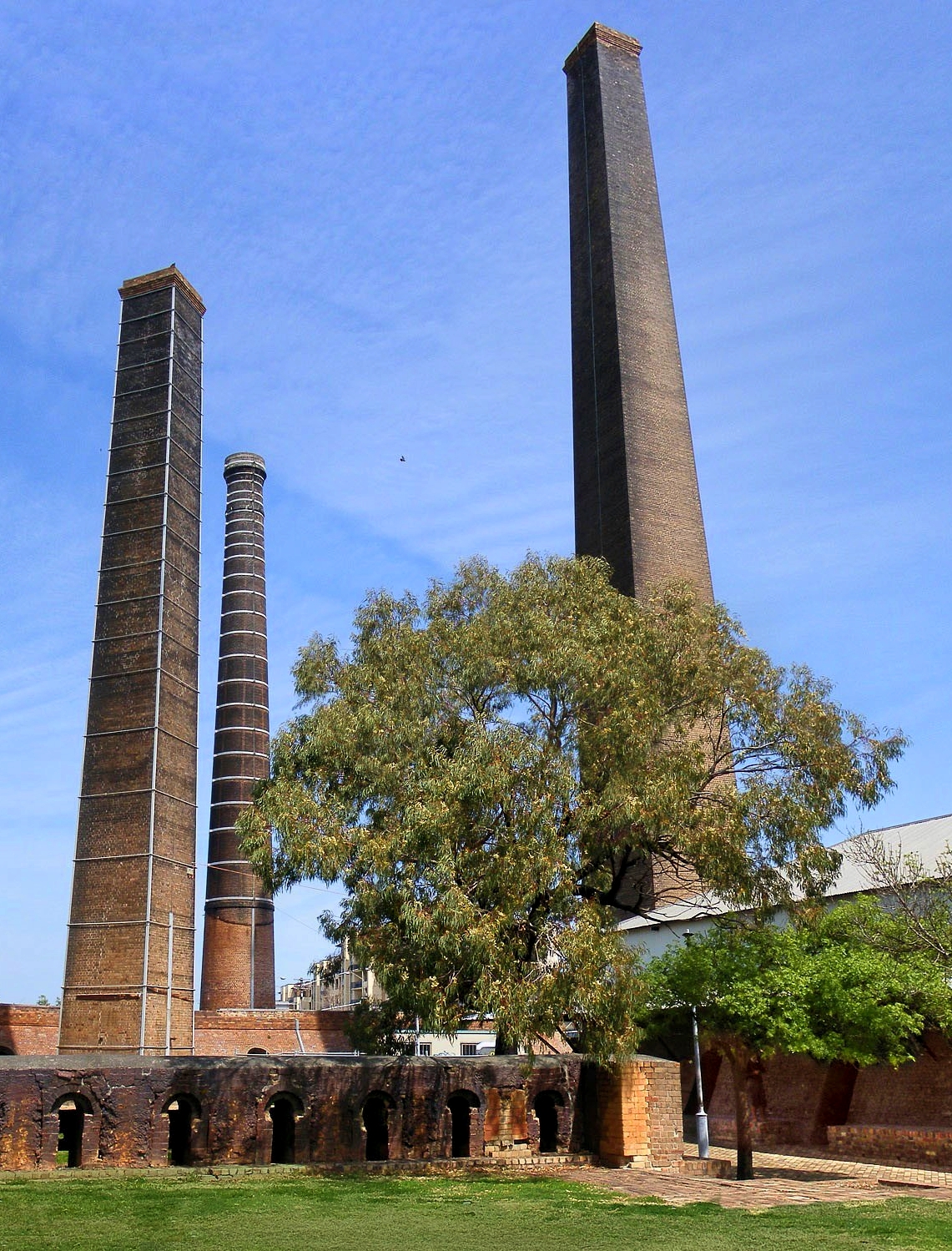 Sydneychimneyssydpark_Fotor a large brick tower with grass and trees