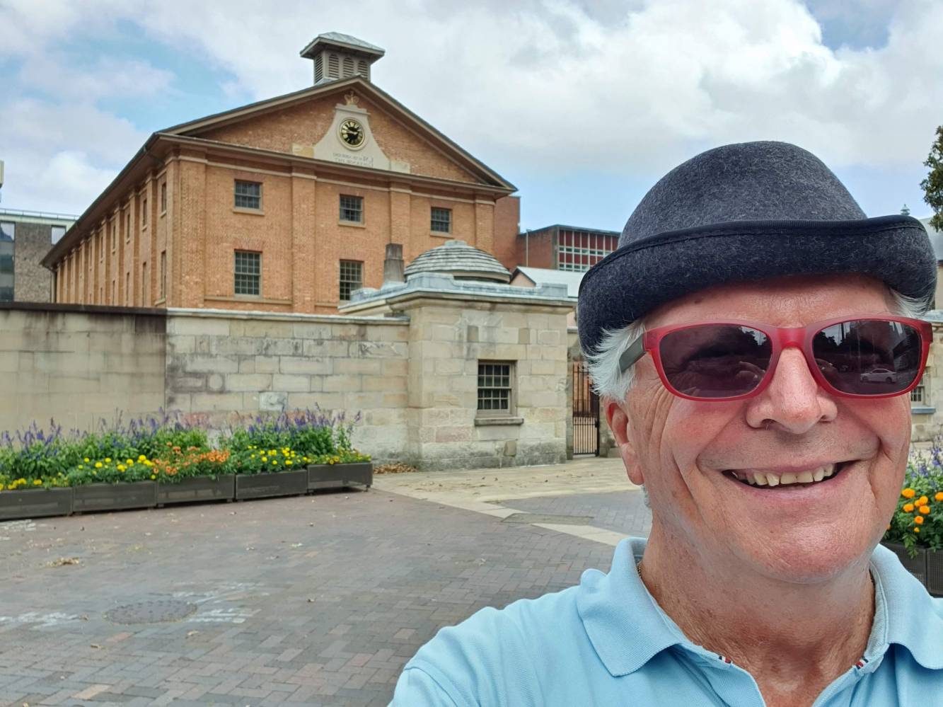 a man wearing a hat and sunglasses Hyde Park Barracksstanding outside of a building